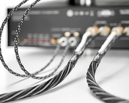 Vier schwarze Kabel, zwei dicke und zwei dünne, angeschlossen an einer Stereoanlage.